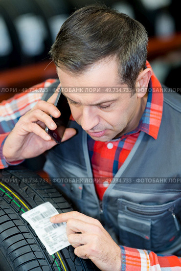male worker looking at sticker showing reference for tyre. Стоковое фото, агентство Ingram Publishing / Фотобанк Лори
