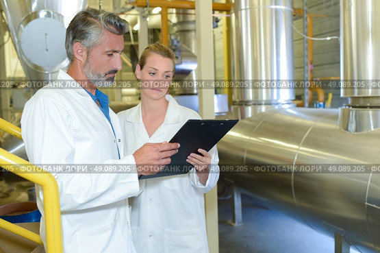 Man and woman looking at clipboard, stood next to metal vat. Стоковое фото, агентство Ingram Publishing / Фотобанк Лори