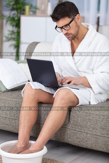 man at home soaking his feet and using a laptop. Стоковое фото, агентство Ingram Publishing / Фотобанк Лори