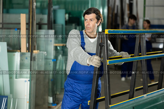Man glazer employee in blue overall works in glass processing shop. Стоковое фото, фотограф Яков Филимонов / Фотобанк Лори
