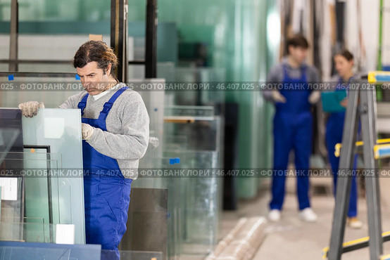 Man glazer employee in blue overall works in glass processing shop. Стоковое фото, фотограф Яков Филимонов / Фотобанк Лори