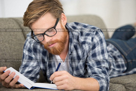 man layed on the sofa writing in a notebook. Стоковое фото, агентство Ingram Publishing / Фотобанк Лори