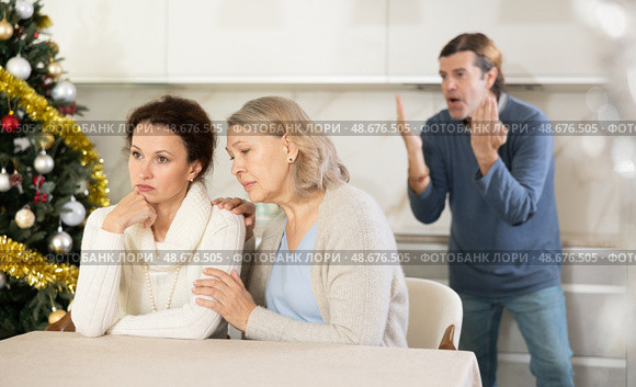 Man on christmas eve quarrels with his wife in kitchen, standing behind her, and elderly mother hugs and calms her daughter. Стоковое фото, фотограф Яков Филимонов / Фотобанк Лори
