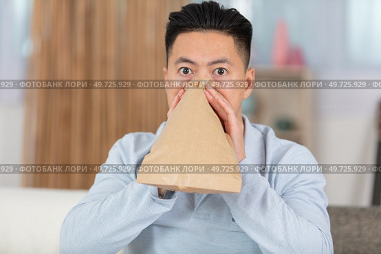 man sitting on sofa vomiting into paper bag at home. Стоковое фото, агентство Ingram Publishing / Фотобанк Лори