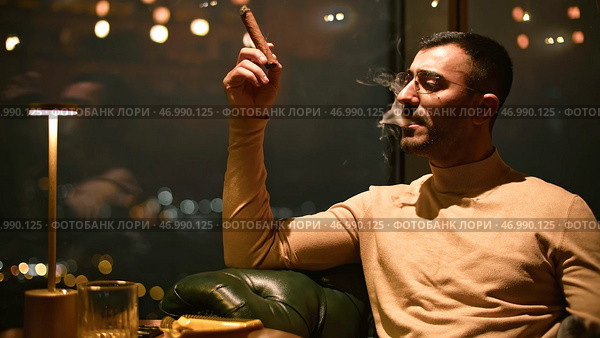 Man smokes cigar in luxury restaurant at night. Стоковое фото, фотограф David Kashakhi / Фотобанк Лори