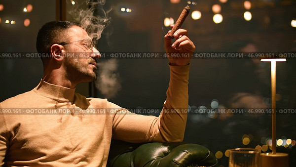 Man smokes cigar in luxury restaurant at night. Стоковое фото, фотограф David Kashakhi / Фотобанк Лори