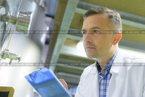 man wearing labcoat inspecting vat and holding clipboard. Стоковое фото, агентство Ingram Publishing / Фотобанк Лори