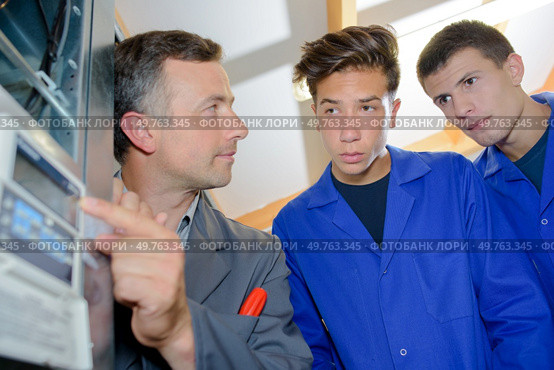 Man with apprentices pointing to thermostatic regulator. Стоковое фото, агентство Ingram Publishing / Фотобанк Лори