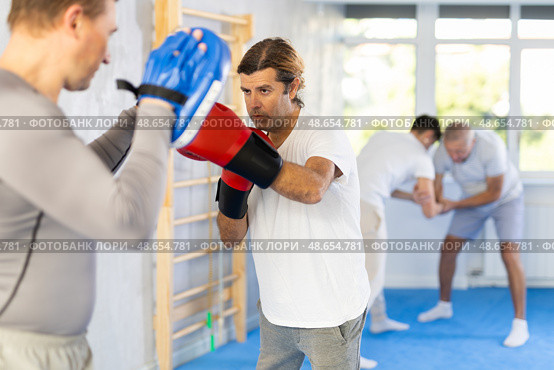 Man works out strength and speed of boxing punch mitts with help of partner in boxing paws. Стоковое фото, фотограф Яков Филимонов / Фотобанк Лори