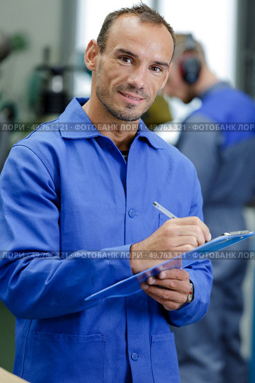 man writing on a clipboard in a garage. Стоковое фото, агентство Ingram Publishing / Фотобанк Лори
