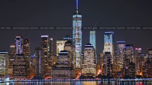 Manhattan skyline glowing at night, One World Trade Center rising above cityscape, illuminating dark waters with dramatic urban reflections and architectural brilliance. Стоковое AI-видео, аниматор Данил Руденко / Фотобанк Лори