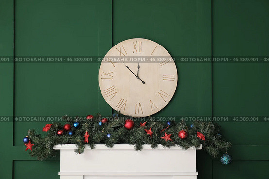 Mantelpiece with Christmas decor and clock on green wall in room. Стоковое фото, фотограф Pixel_shot / Фотобанк Лори