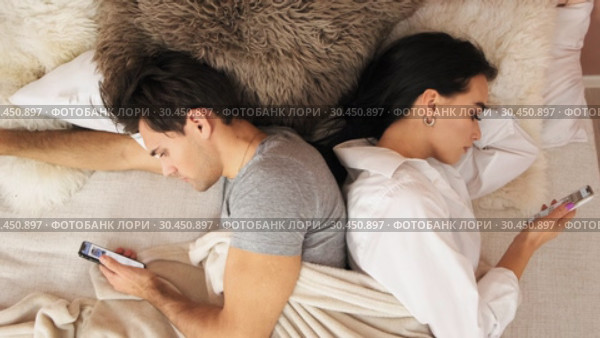 Married couple lies back to back in bed with mobile phones. Slow motion. Стоковое видео, видеограф Denis Mishchenko / Фотобанк Лори