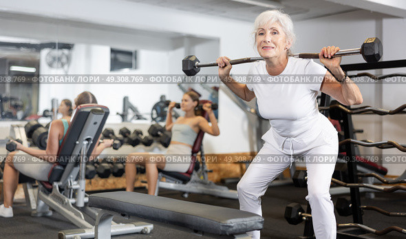 Mature sportswoman doing exercises with a barbell and dumbbells in gym. Стоковое фото, фотограф Яков Филимонов / Фотобанк Лори