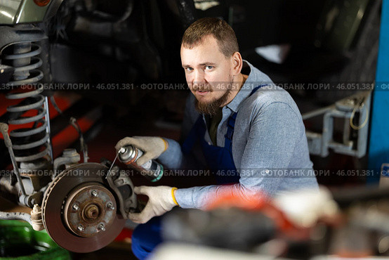 Mechanic applying anti-rust liquid to bolts on car wheel hub. Стоковое фото, фотограф Яков Филимонов / Фотобанк Лори
