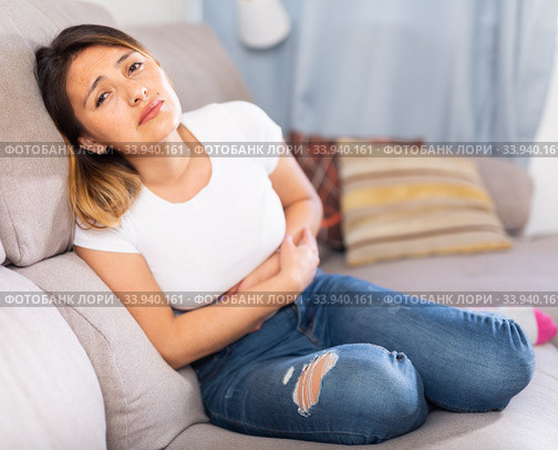 Mexican female at sofa holding hands on the illness stomache. Стоковое фото, фотограф Яков Филимонов / Фотобанк Лори