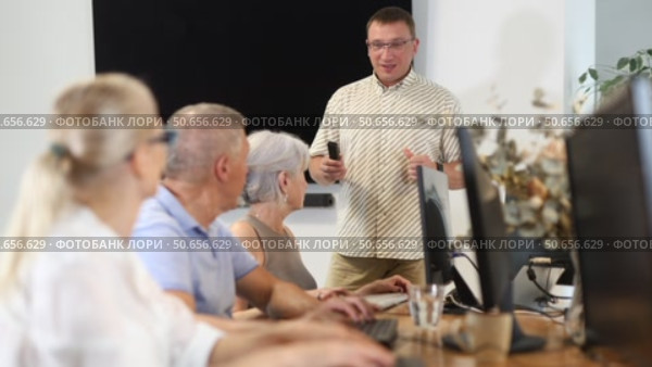 Middle-aged male instructor teaching computer skills to old students during IT classes. Стоковое видео, видеограф Яков Филимонов / Фотобанк Лори