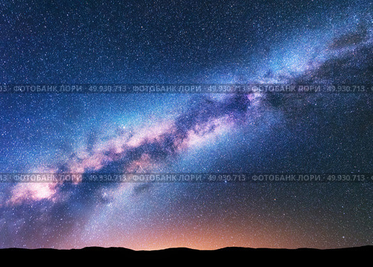 Milky Way. Fantastic night landscape with purple milky way, sky full of stars, yellow light and hills. Shiny stars. Beautiful scene with universe. Space background with starry sky. Astrophotography. Стоковое фото, агентство Ingram Publishing / Фотобанк Лори