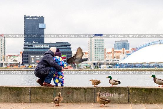 Minsk, Belarus - January 07, 2019: Mother and child on the banks of the river. Waterfront, birds. Редакционное фото, фотограф Denis Shitikoff / Фотобанк Лори