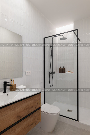 Modern bathroom with a glass shower, wooden vanity, and minimalist decor. Neutral colors create a clean and spacious atmosphere. Стоковое фото, фотограф PAv / Фотобанк Лори