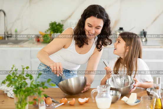 Mom and girl are talking in kitchen and mixing ingredients for pastry in bowl with whisk. Стоковое фото, фотограф Яков Филимонов / Фотобанк Лори