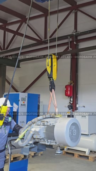 Moscow, Russia july 3, 2025. Factory worker guides an overhead crane lifting a large engine. Редакционное видео, видеограф Юрий Поздников / Фотобанк Лори