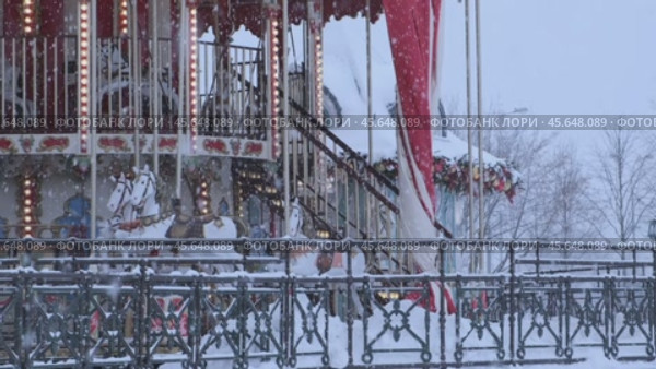 Москва, Россия - 07 декабря 2024 г.: Карусель на площадке фестиваля "Московские сезоны" в Люблино. Крупный план детского аттракциона с лошадками и новогодними огнями. Сильный снегопад. Замедленная съемка. Редакционное видео, видеограф Светлана Ельцова / Фотобанк Лори
