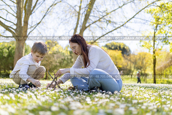 Mother and son building a small teepee with branches in a field of daisies. Стоковое фото, фотограф Константин Шишкин / Фотобанк Лори