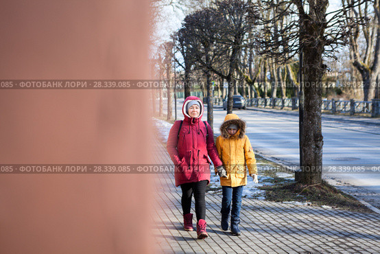 Mother in red jacket and young daughter in yellow walking on urban street, view from the corner. Стоковое фото, фотограф Кекяляйнен Андрей / Фотобанк Лори