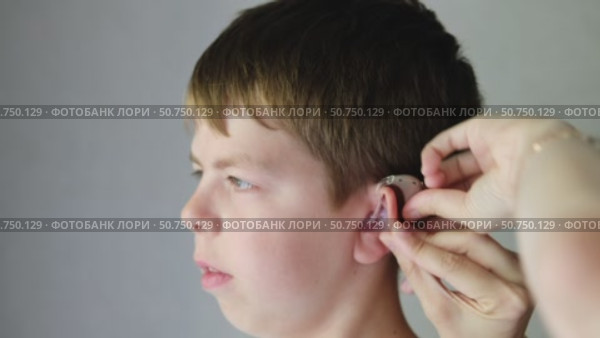 Mother puts hearing aid with individual plastic earmolds on the ear of an 10 year old boy. Sensorineural hearing loss of a little boy. Стоковое видео, видеограф Кашапова Эльвира / Фотобанк Лори