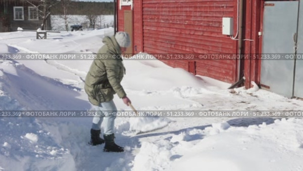 Moving snow with manual snow shovel by individual dressed in winter clothing standing beside large snow pile near rural house. Стоковое видео, видеограф Владимир Григорьев / Фотобанк Лори