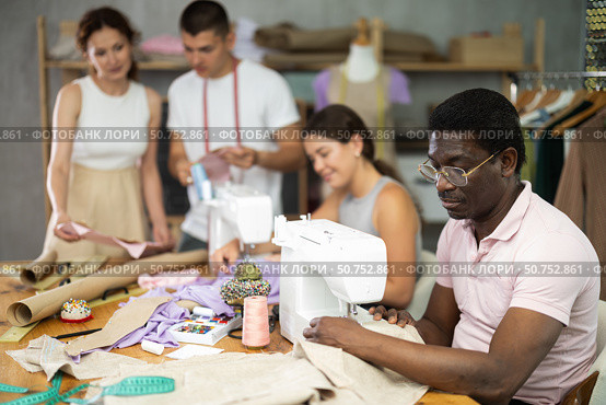 Multiethnic participants in coterie practice sewing, chatting, work textile and paper dress pattern. Стоковое фото, фотограф Яков Филимонов / Фотобанк Лори