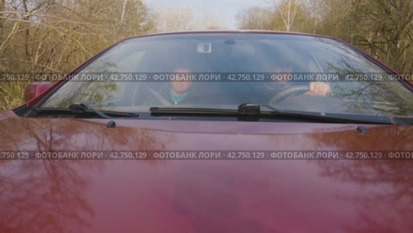 Мужчина и женщина едут в автомобиле по проселочной дороге. Мужчина за рулем автомобиля. Камера установлена на капоте автомобиля. Дорога проходит через лес. Люди разговаривают во время поездки в машине. Стоковое видео, видеограф Воловодов Владимир / Фотобанк Лори