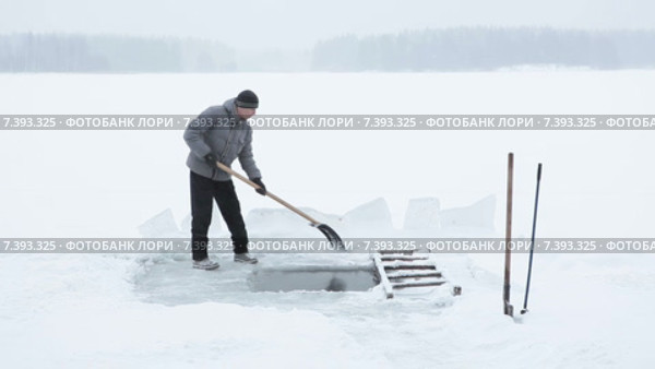 Мужчина очищает прорубь для зимнего купания от наледи лопатой. Лесное озеро. Стоковое видео, видеограф Кекяляйнен Андрей / Фотобанк Лори