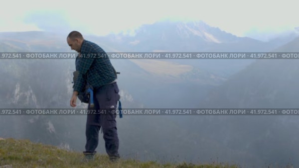 Мужчина-пешеход в клетчатой флисовой куртке снимает со спины рюкзак. На заднем плане - ущелье и заснеженные вершины гор. Концепция пешего туризма. Стоковое видео, видеограф Воловодов Владимир / Фотобанк Лори