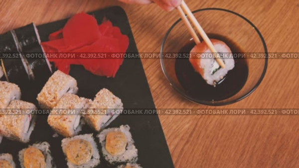 Набор вкусных японских суши-роллов на каменной черной доске. Вид сверху. Палочки для еды берут суши из набора и макают их в соевый соус. Различные виды суши с красной икрой, рыбой, сыром "Филадельфия" и палочками для еды. Стоковое видео, видеограф Воловодов Владимир / Фотобанк Лори