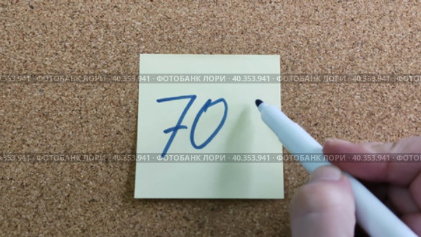 Надпись 70% на бумажном стикере приклеенном к пробковой  доске. Женщина пишет маркером на желтой бумаге. Синий фломастер в женской руке. Рукописный текст красивым почерком. Процент скидки или прибыли. The inscription is 70% on a paper sticker glued to a cork board. A woman writes with a marker on yellow paper. A blue felt-tip pen in a woman's hand. Handwritten text in a beautiful handwriting. Percentage of discount or profit. Стоковое видео, видеограф Ирина / Фотобанк Лори