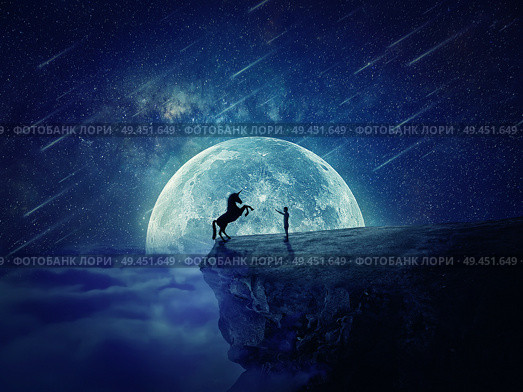 Night scene with a boy standing at the edge of a cliff chasm trying to tame a wild unicorn. Begining of a new friendship, fearless symbol. Стоковое фото, агентство Ingram Publishing / Фотобанк Лори