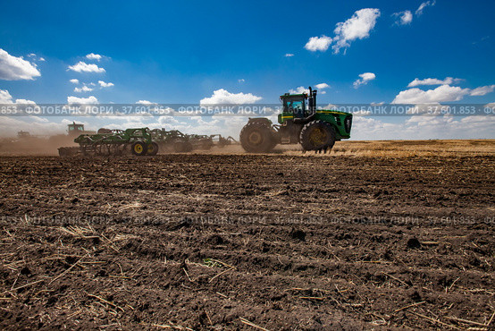 North Kazakhstan Province, Kazakhstan - May 12, 2012: Spring sowing campaign. John Deere tractors cultivating soil with harrow.Blue sky, clouds. Редакционное фото, фотограф Alexey Rezvykh / Фотобанк Лори
