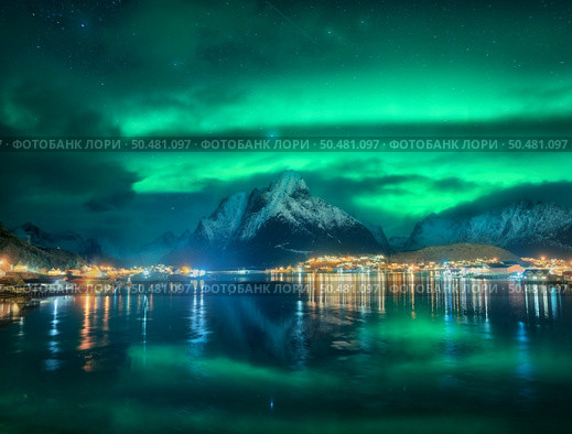 Northern lights in Reine, Lofoten Islands, Norway. Starry sky and Aurora borealis, snowy mountains, sea coast, houses, rocks, reflection in water, city lights at winter night. Bright polar lights. Стоковое фото, агентство Ingram Publishing / Фотобанк Лори