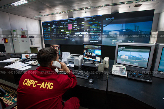 Oil refinery plant. Operation control center and operator in red work wear looks on monitors. CNPC company. (2012 год). Редакционное фото, фотограф Alexey Rezvykh / Фотобанк Лори