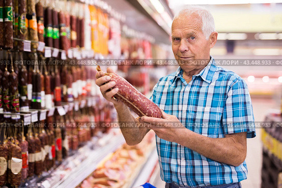 Old age man examines salami in sausage department of supermarket. Стоковое фото, фотограф Татьяна Яцевич / Фотобанк Лори