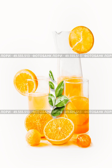 Orange juice in glasses and jug with slices and green leaves at white background. Healthy drinks. Summer beverages. Refreshing. Vitamin C. Стоковое фото, агентство Ingram Publishing / Фотобанк Лори