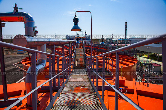 Orange steel storage tanks with acid at sulfuric (sulphuric) acid plant warehouse. Grid floor on the roof and lamp on blue sky. Стоковое фото, фотограф Alexey Rezvykh / Фотобанк Лори