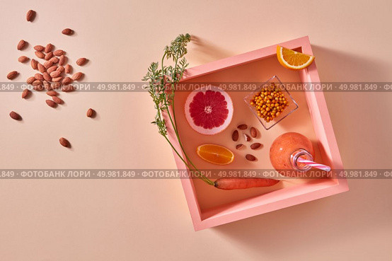 Organic drink with sea buckthorn, almonds, citrus fruits in glass on an orange paper in square frame. Healthy dietary food. Flat lay.. Homemade natural organic smoothie, made with grapefruits, orange, berries, carrots and nuts in glass bottle on an orange paper background. Стоковое фото, агентство Ingram Publishing / Фотобанк Лори
