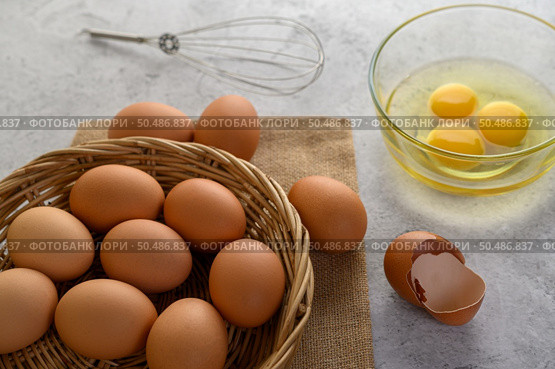 Organic eggs on sack cloth, many eggs on wicker basket and glasses bowl, oil and egg whisk placed on the floor, preparing for cooking food or dessert, copy space. Стоковое фото, агентство Ingram Publishing / Фотобанк Лори