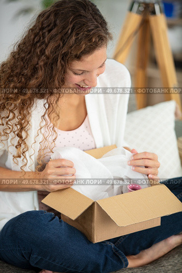 overjoyed woman seated on sofa open parcel. Стоковое фото, агентство Ingram Publishing / Фотобанк Лори