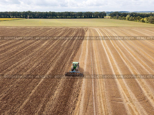 Panoramic view of tractor plowing the soil after harvesting on the field. Aerial view from the drone of the field after harvest. Preparatory work for sowing crops, cultivation of the soil by a tractor after harvesting in the summer time. Стоковое фото, агентство Ingram Publishing / Фотобанк Лори