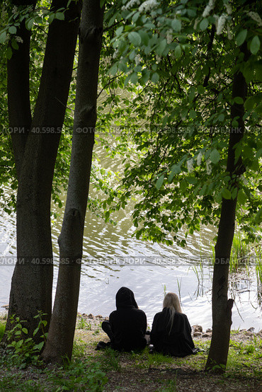 Парень и девушка в темной одежде сидят на берегу пруда у кромки воды под цветущей черемухой спиной к зрителю. Стоковое фото, фотограф Наталья Николаева / Фотобанк Лори