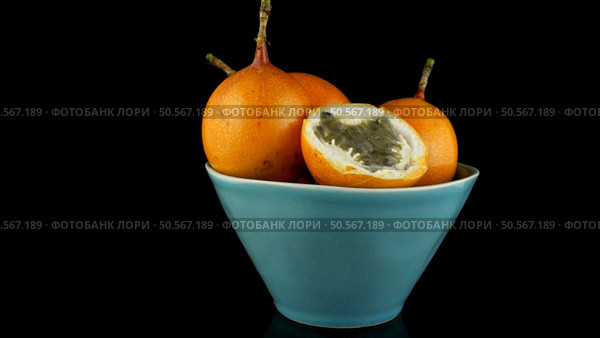Passion fruit maracuja granadilla on ceramic blue bowl, black background. Стоковое фото, агентство Ingram Publishing / Фотобанк Лори